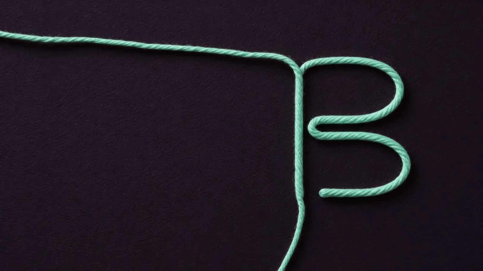 Fio verde-menta desenhando a letra B do símbolo da Balkan sobre papel berinjela.